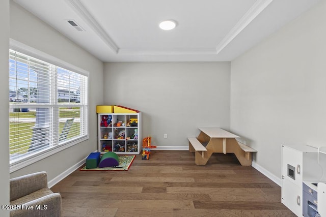 rec room with baseboards, a tray ceiling, wood finished floors, and visible vents