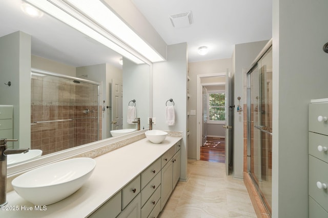 full bath featuring visible vents, a sink, double vanity, and a stall shower