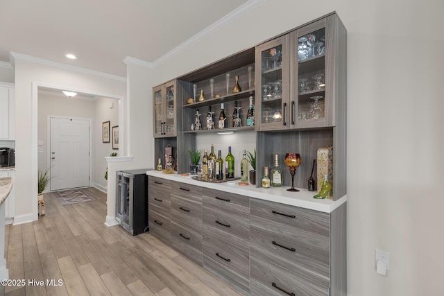 bar with crown molding, light hardwood / wood-style floors, and beverage cooler