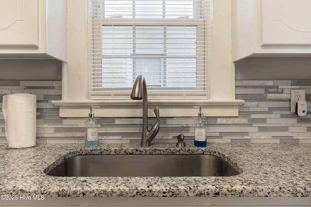 room details featuring white cabinetry, sink, light stone counters, and backsplash