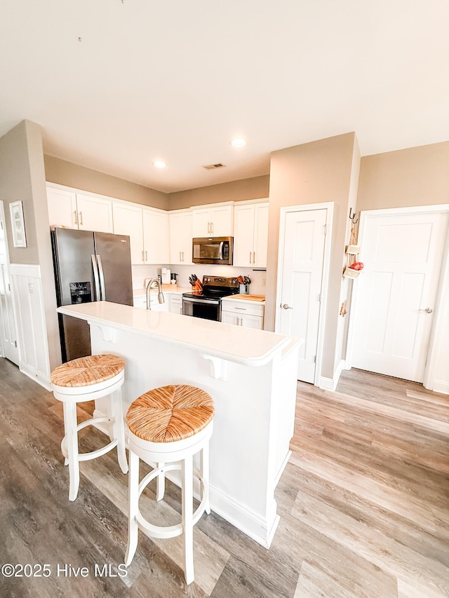 kitchen with white cabinetry, appliances with stainless steel finishes, a center island with sink, and a kitchen bar