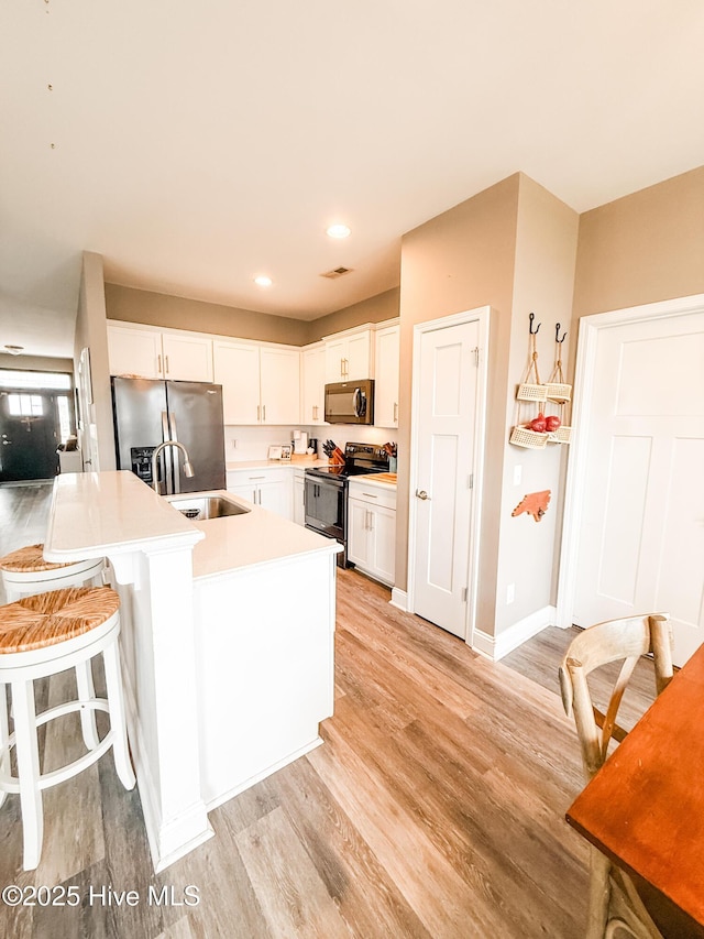 kitchen featuring a breakfast bar, sink, white cabinets, stainless steel appliances, and light hardwood / wood-style flooring