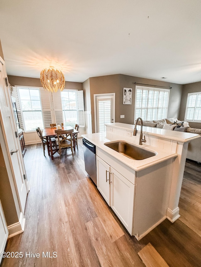 kitchen featuring sink, dishwasher, white cabinetry, a center island with sink, and light wood-type flooring