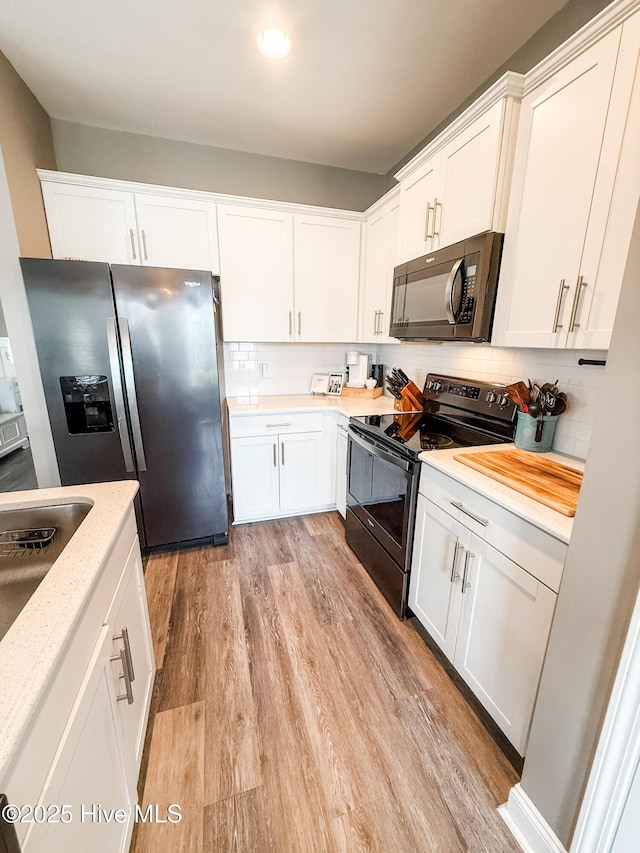 kitchen featuring tasteful backsplash, white cabinetry, stainless steel appliances, light stone countertops, and light hardwood / wood-style flooring