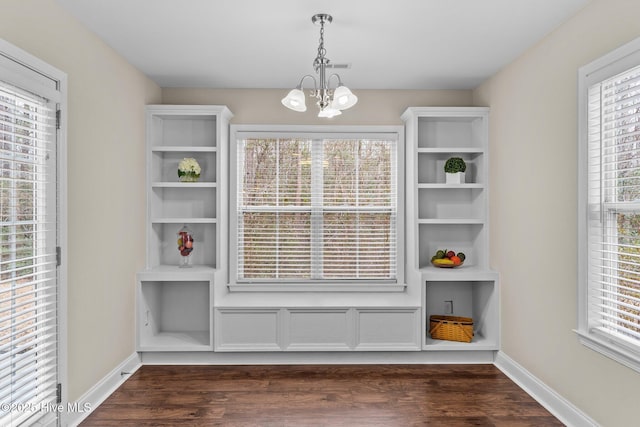 unfurnished dining area with built in shelves, dark wood-type flooring, a chandelier, and a healthy amount of sunlight