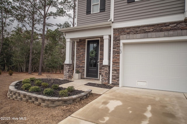 doorway to property with driveway, stone siding, and an attached garage