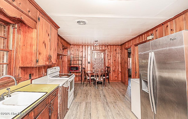 kitchen with sink, wood walls, stainless steel fridge with ice dispenser, light wood-type flooring, and white electric stove