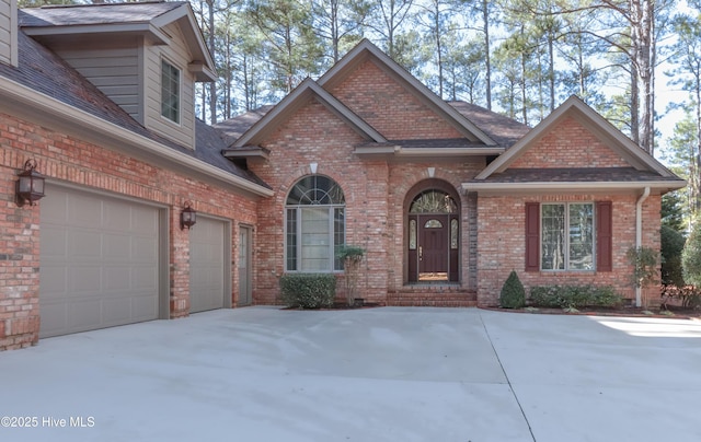 view of front of property featuring a garage, driveway, a shingled roof, and brick siding