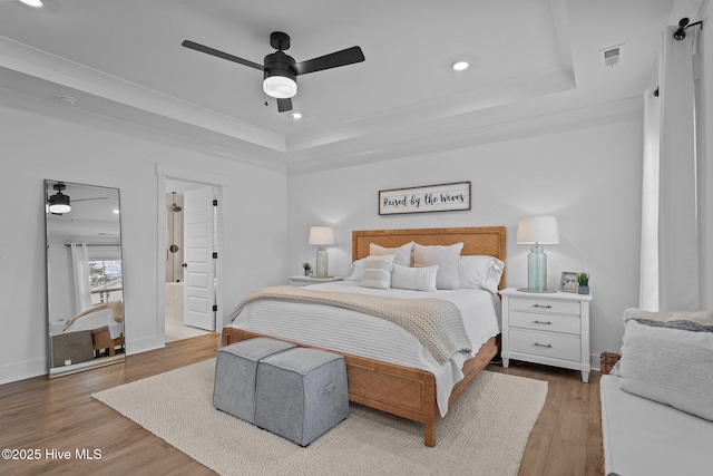 bedroom featuring ceiling fan, ornamental molding, wood-type flooring, and a tray ceiling