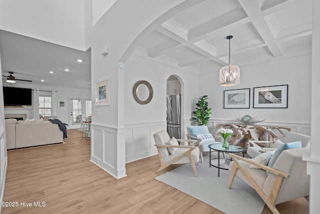 living room with beamed ceiling, coffered ceiling, ceiling fan with notable chandelier, and light wood-type flooring