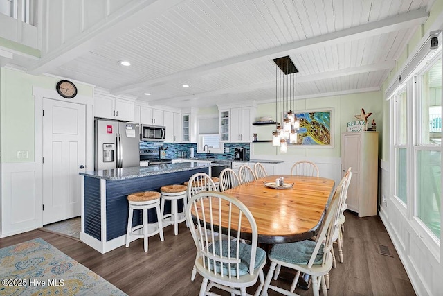 dining space featuring beam ceiling, plenty of natural light, and dark wood finished floors