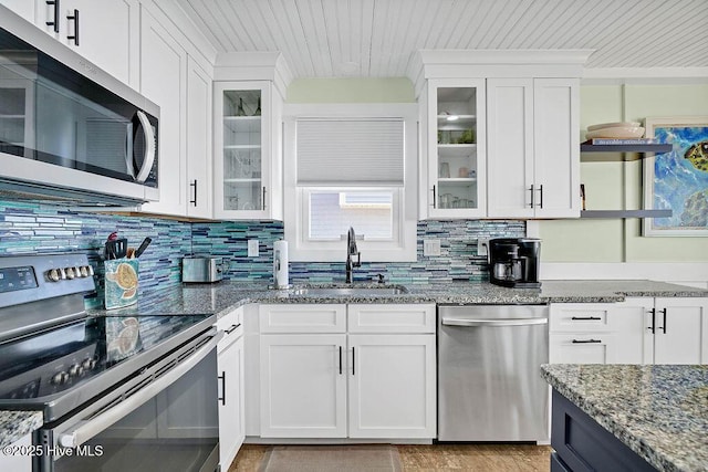 kitchen featuring tasteful backsplash, dark stone counters, stainless steel appliances, white cabinetry, and a sink