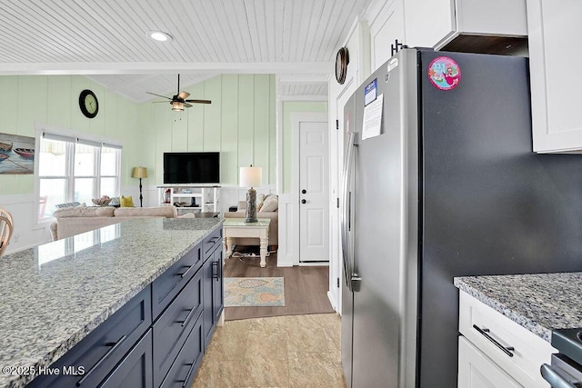 kitchen featuring light stone countertops, white cabinetry, freestanding refrigerator, and vaulted ceiling