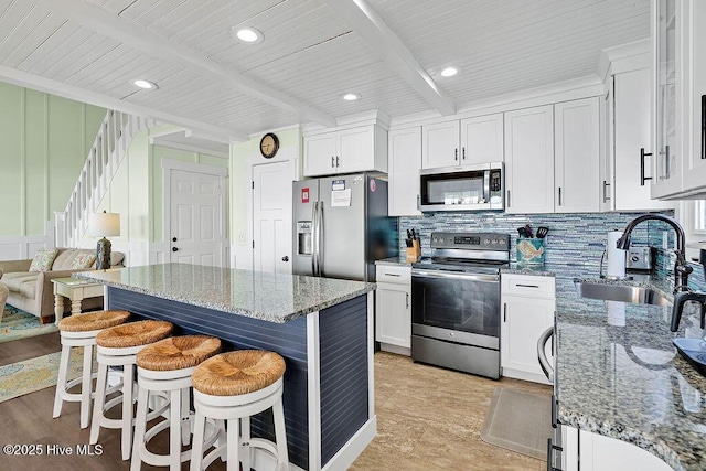 kitchen featuring beam ceiling, a sink, backsplash, stainless steel appliances, and a breakfast bar area