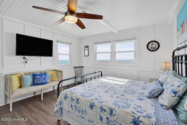 bedroom featuring a ceiling fan, beam ceiling, a decorative wall, and wood finished floors