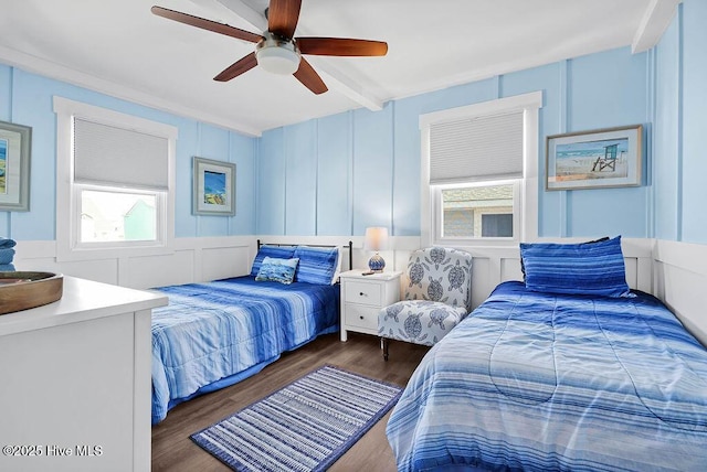 bedroom with beamed ceiling, wood finished floors, a ceiling fan, and a decorative wall