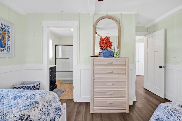 bedroom with beam ceiling, ornamental molding, dark wood-type flooring, a decorative wall, and connected bathroom