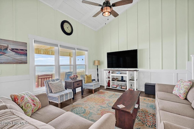 living room with wood finished floors, beamed ceiling, high vaulted ceiling, ceiling fan, and a decorative wall