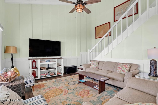 living room featuring a decorative wall, stairway, ceiling fan, and wood finished floors