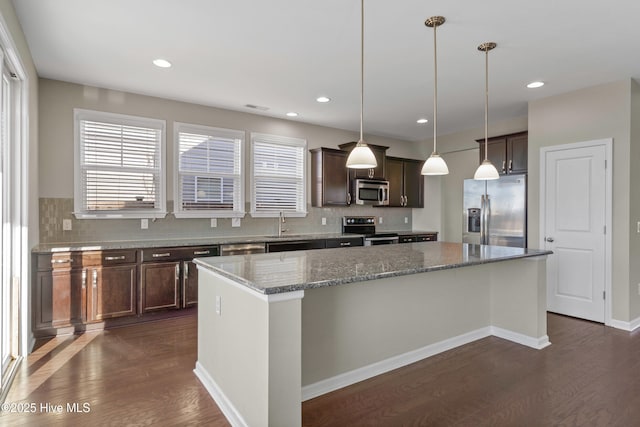 kitchen featuring appliances with stainless steel finishes, dark wood-type flooring, a kitchen island, and decorative backsplash