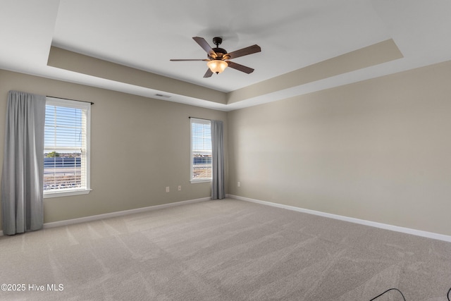 unfurnished room with light carpet, a tray ceiling, and baseboards