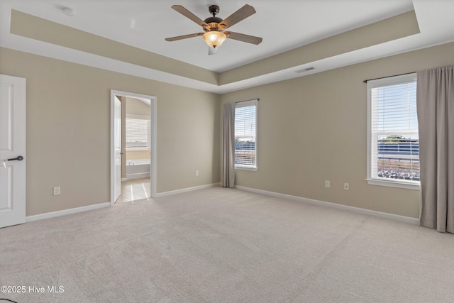 unfurnished room with a tray ceiling, visible vents, light carpet, and baseboards