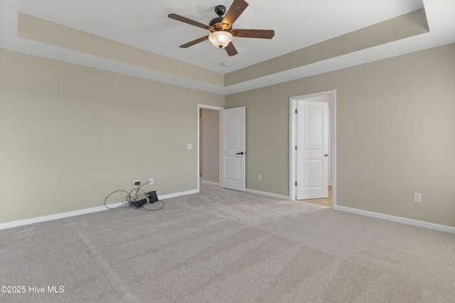 unfurnished room with light carpet, a tray ceiling, a ceiling fan, and baseboards