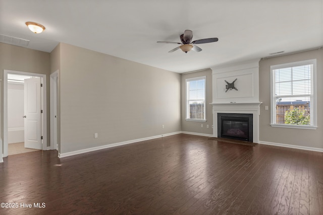 unfurnished living room featuring dark wood-style flooring, plenty of natural light, a glass covered fireplace, and visible vents