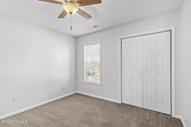 unfurnished bedroom with a textured ceiling, a closet, light colored carpet, and ceiling fan