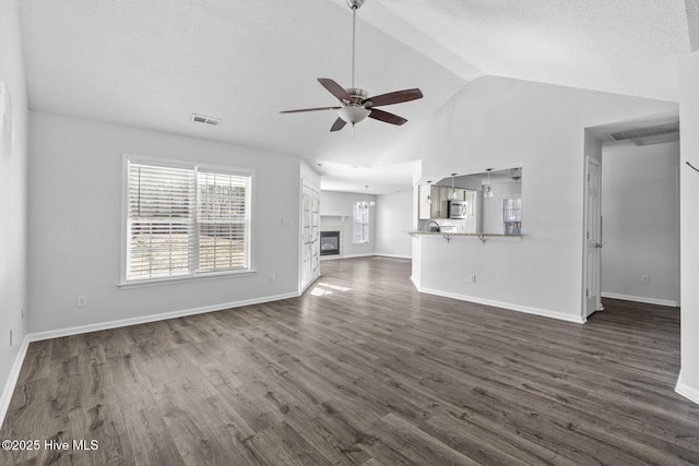 unfurnished living room featuring ceiling fan, dark wood-type flooring, a textured ceiling, and lofted ceiling