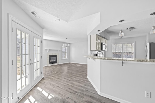 kitchen with kitchen peninsula, appliances with stainless steel finishes, white cabinetry, and decorative light fixtures