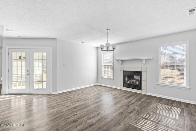 unfurnished living room with a fireplace, french doors, a notable chandelier, wood-type flooring, and a textured ceiling