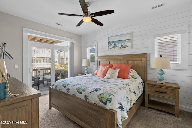 carpeted bedroom featuring ceiling fan, access to exterior, and wood walls