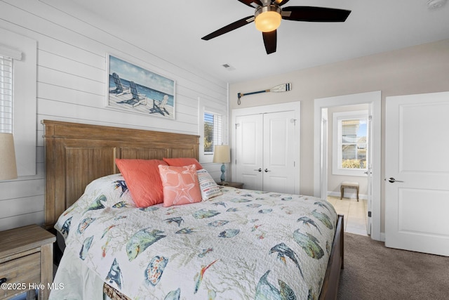 bedroom with carpet flooring, wooden walls, ceiling fan, and a closet