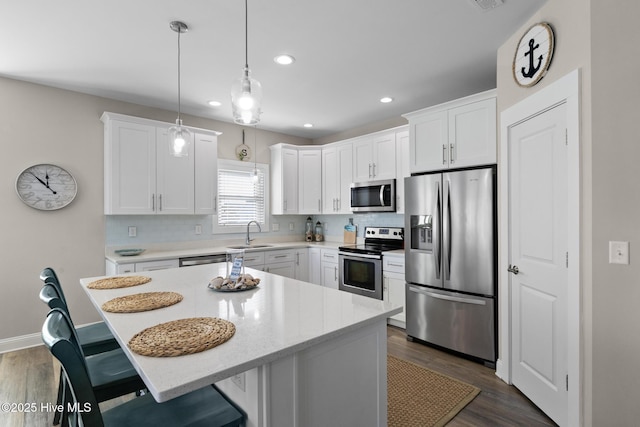 kitchen with appliances with stainless steel finishes, decorative light fixtures, white cabinets, backsplash, and a center island