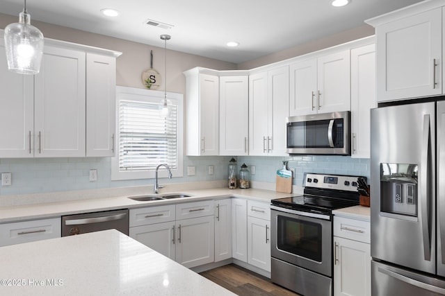 kitchen with sink, tasteful backsplash, hanging light fixtures, appliances with stainless steel finishes, and white cabinets