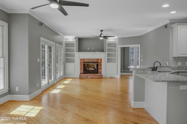 unfurnished living room featuring ornamental molding, a brick fireplace, sink, and light hardwood / wood-style flooring