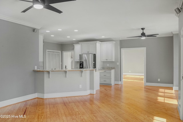 kitchen featuring stainless steel refrigerator with ice dispenser, a kitchen bar, white cabinetry, crown molding, and kitchen peninsula