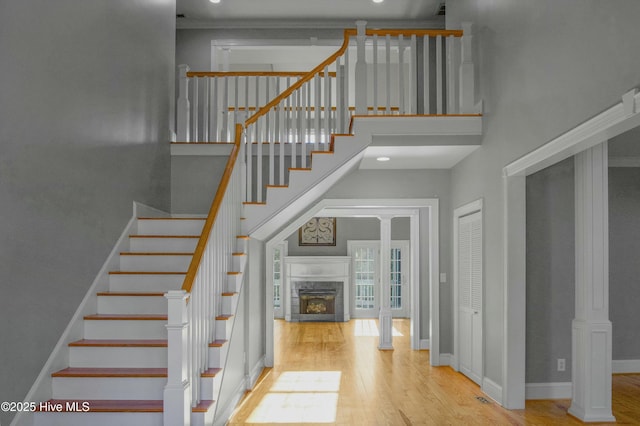 stairway featuring wood-type flooring, a high ceiling, and ornate columns