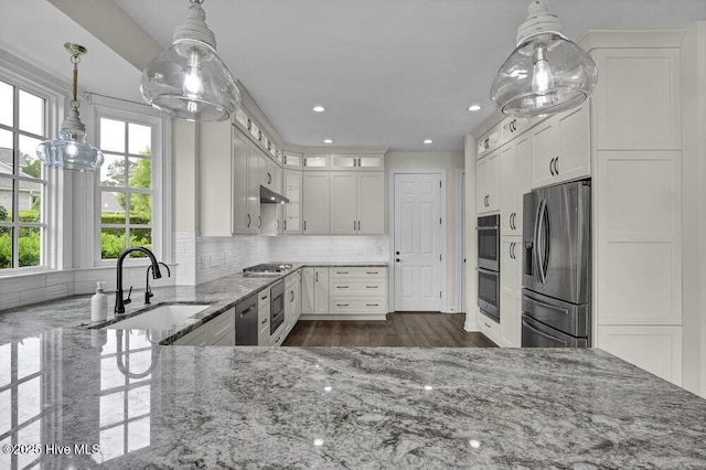 kitchen with under cabinet range hood, light stone counters, a sink, appliances with stainless steel finishes, and backsplash