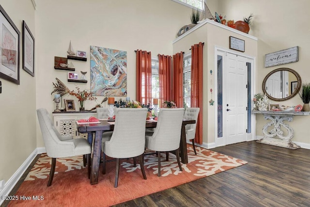 dining room with a towering ceiling, wood-type flooring, and a healthy amount of sunlight