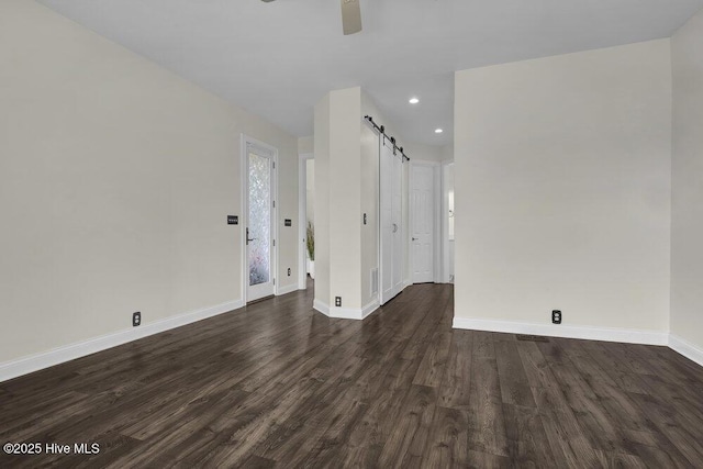 spare room with baseboards, a barn door, dark wood finished floors, and recessed lighting