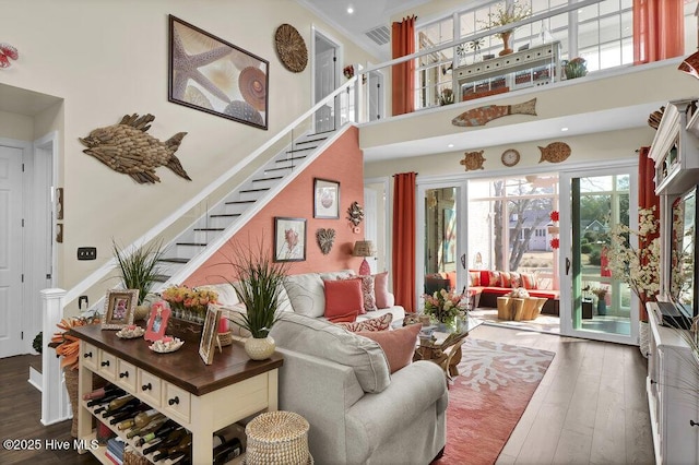 living area with visible vents, wood finished floors, stairway, and a towering ceiling