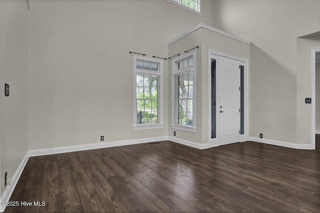 unfurnished room with baseboards, dark wood finished floors, a towering ceiling, and visible vents