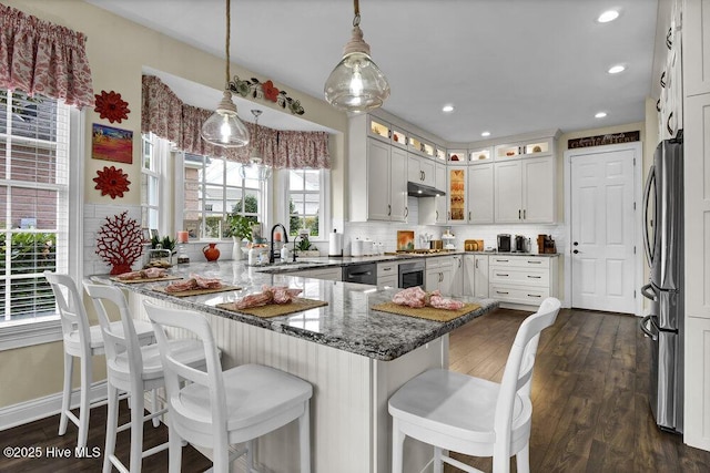 kitchen with a peninsula, glass insert cabinets, stone countertops, a sink, and stainless steel appliances