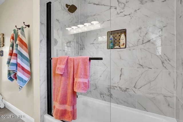 bathroom featuring baseboards and bath / shower combo with glass door