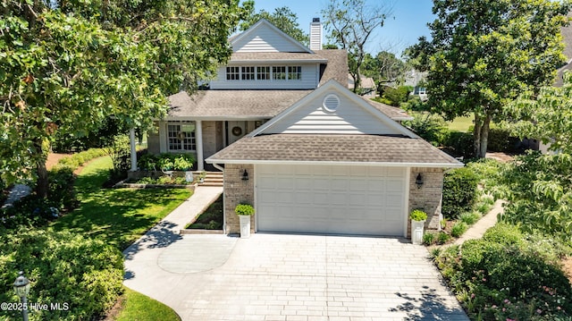 view of front of property with a chimney, brick siding, decorative driveway, an attached garage, and a shingled roof
