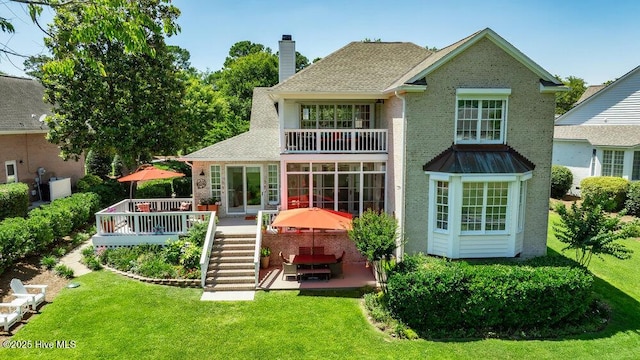 rear view of property featuring a balcony, a patio, a chimney, a lawn, and stairway