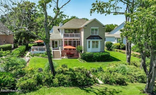 back of property featuring a chimney, a deck, a patio area, a balcony, and a yard