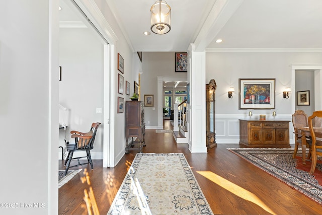 foyer with dark wood-type flooring, a decorative wall, a wainscoted wall, and ornamental molding